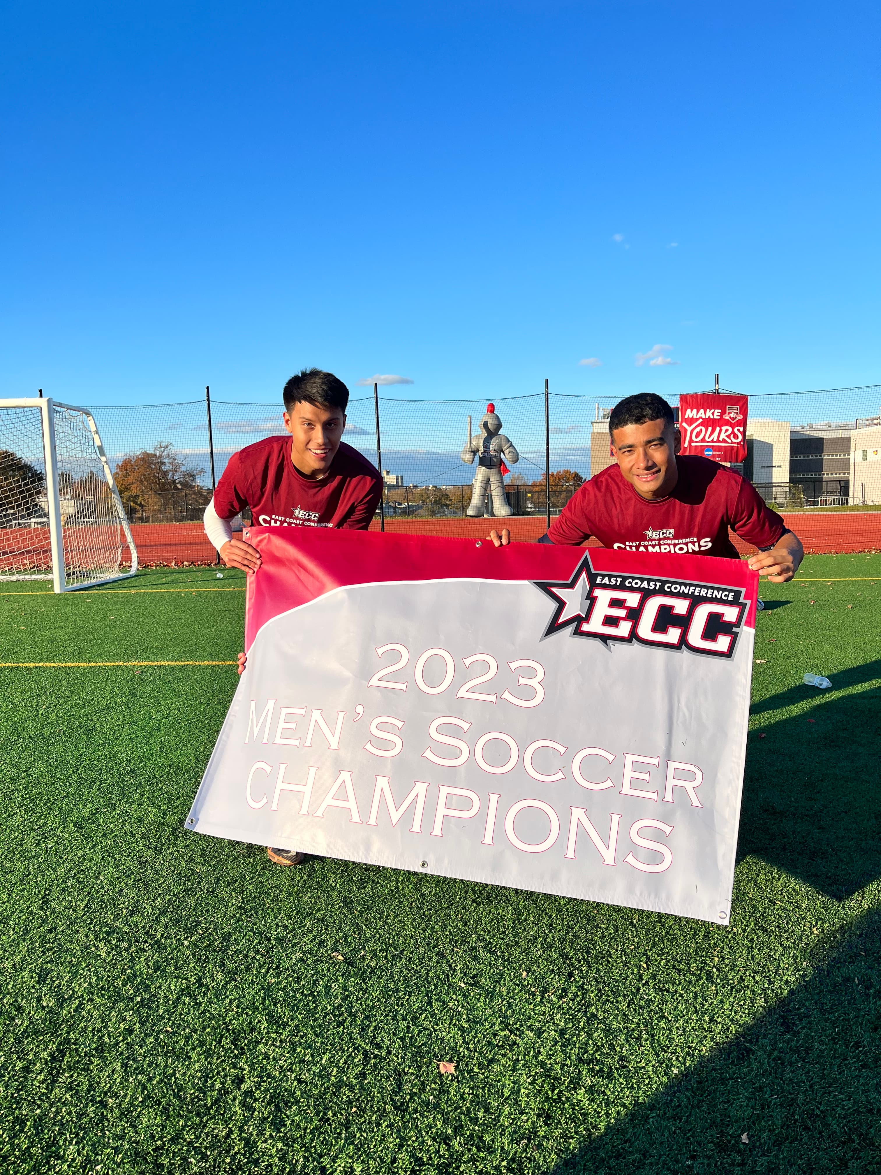Pepe holding the 2023 East Coast Conference Men's Soccer Champions banner